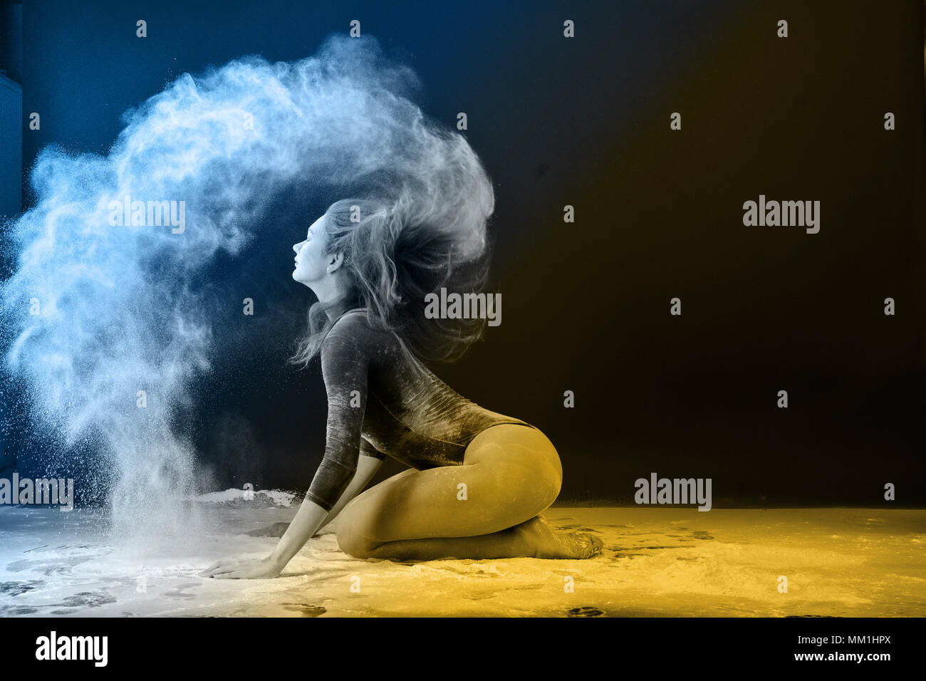 Slender girl dancing in white dust, Studio shot. Illuminated with colored lanterns. Blue and mustard on black background Stock Photo