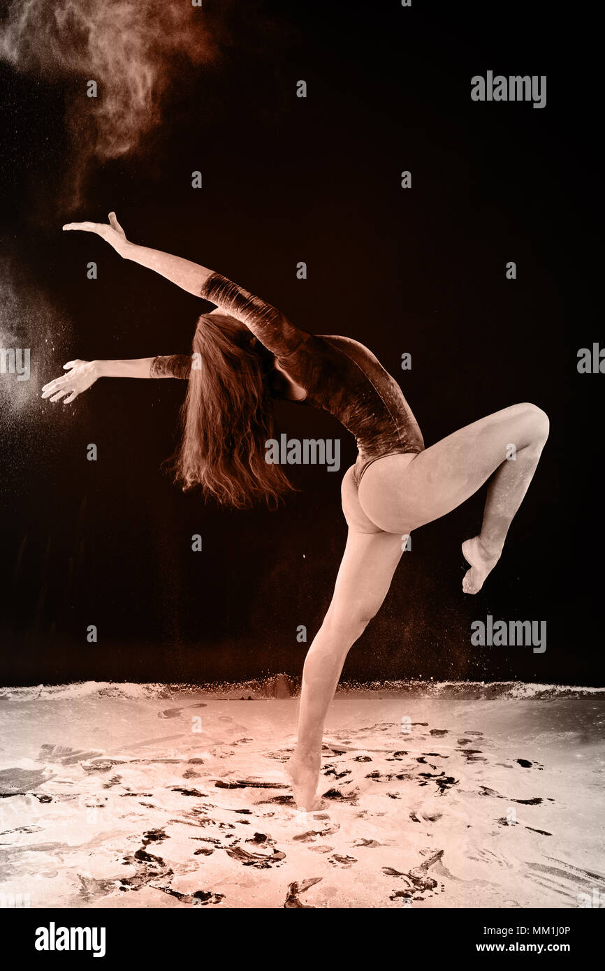 Slender girl dancing in white dust, Studio shot. Illuminated with colored lanterns. Blue and green on black background Stock Photo