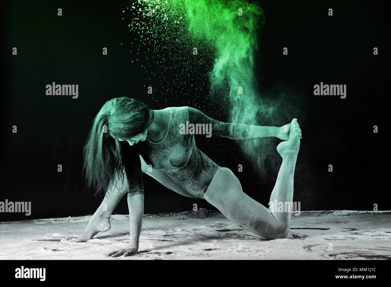 Slender girl dancing in white dust, Studio shot. Illuminated with colored lanterns. Blue and green on black background Stock Photo