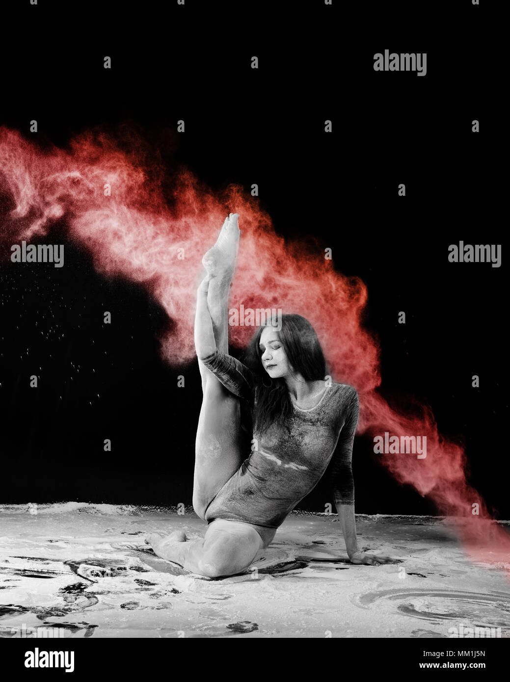 Girl doing gymnastic exercises in a cloud of red dust on a black background Stock Photo