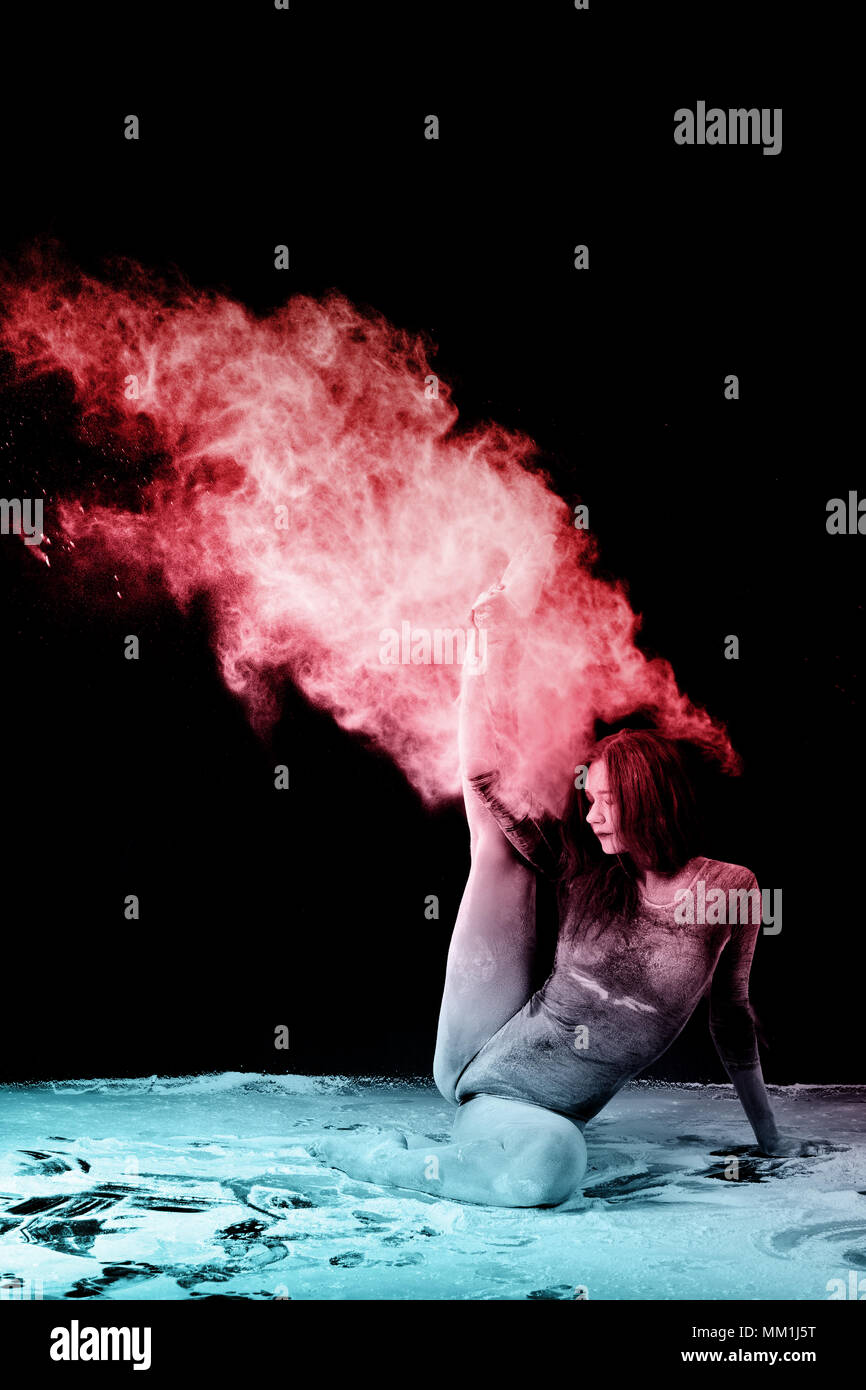 Girl doing gymnastic exercises in a cloud of red dust on a black background.Ice and flame. Gymnastics and dust clouds. Stock Photo