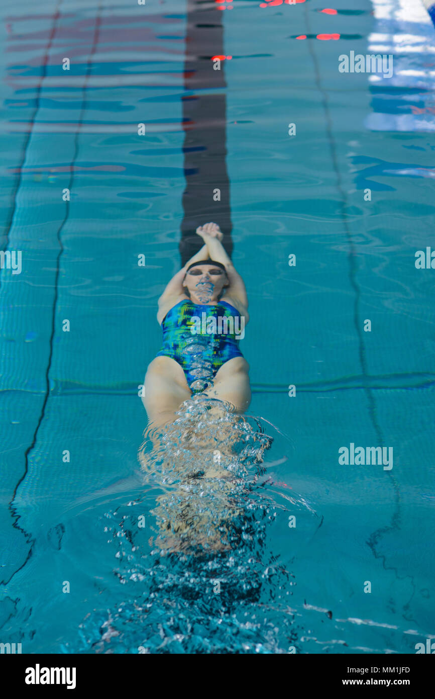 Woman swimmer swims on her back in the center of her track in the pool Stock Photo
