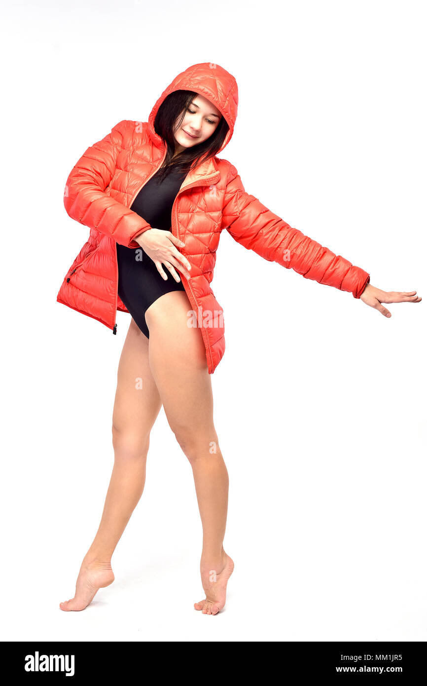 A woman gymnast in a black sporty swimming suit and a red winter jacket is doing stretching exercises (isolation on white) Stock Photo