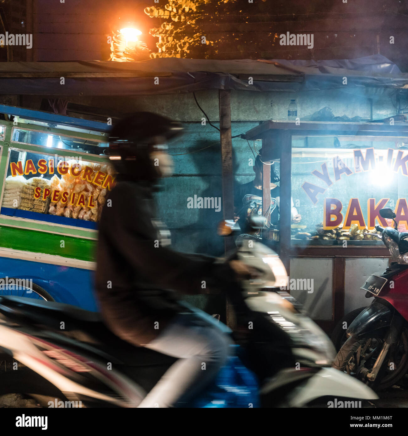 Man riding a scooter on a street with food stalls in a poor district of Jakarta Stock Photo