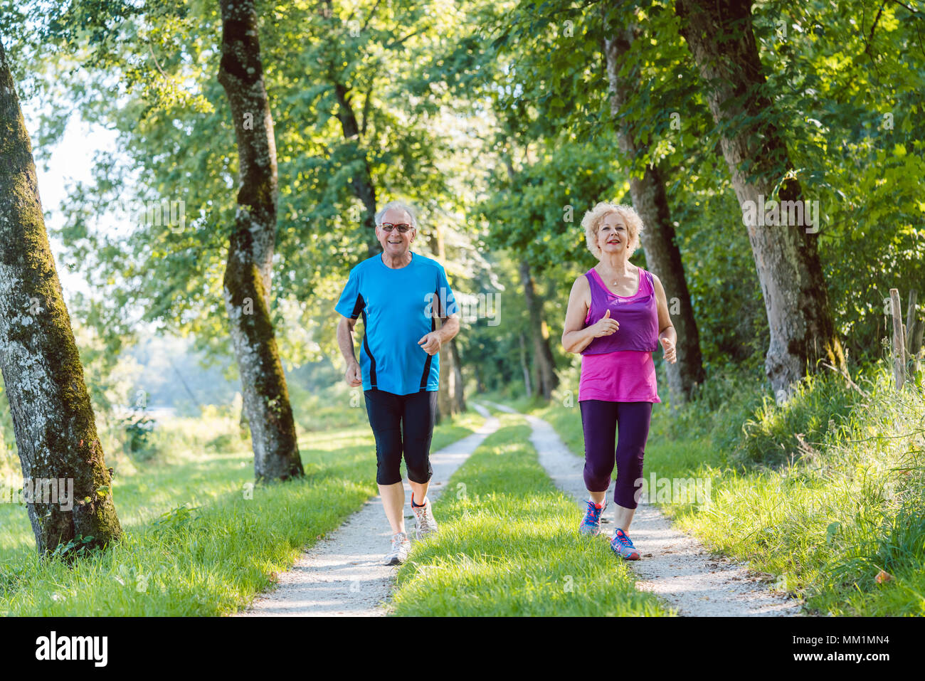 Two active seniors with a healthy lifestyle smiling while jogging together Stock Photo