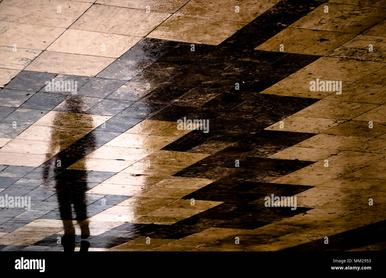 Blurry reflection shadow of one person walking the city street patterned sidewalk on a  rainy day Stock Photo