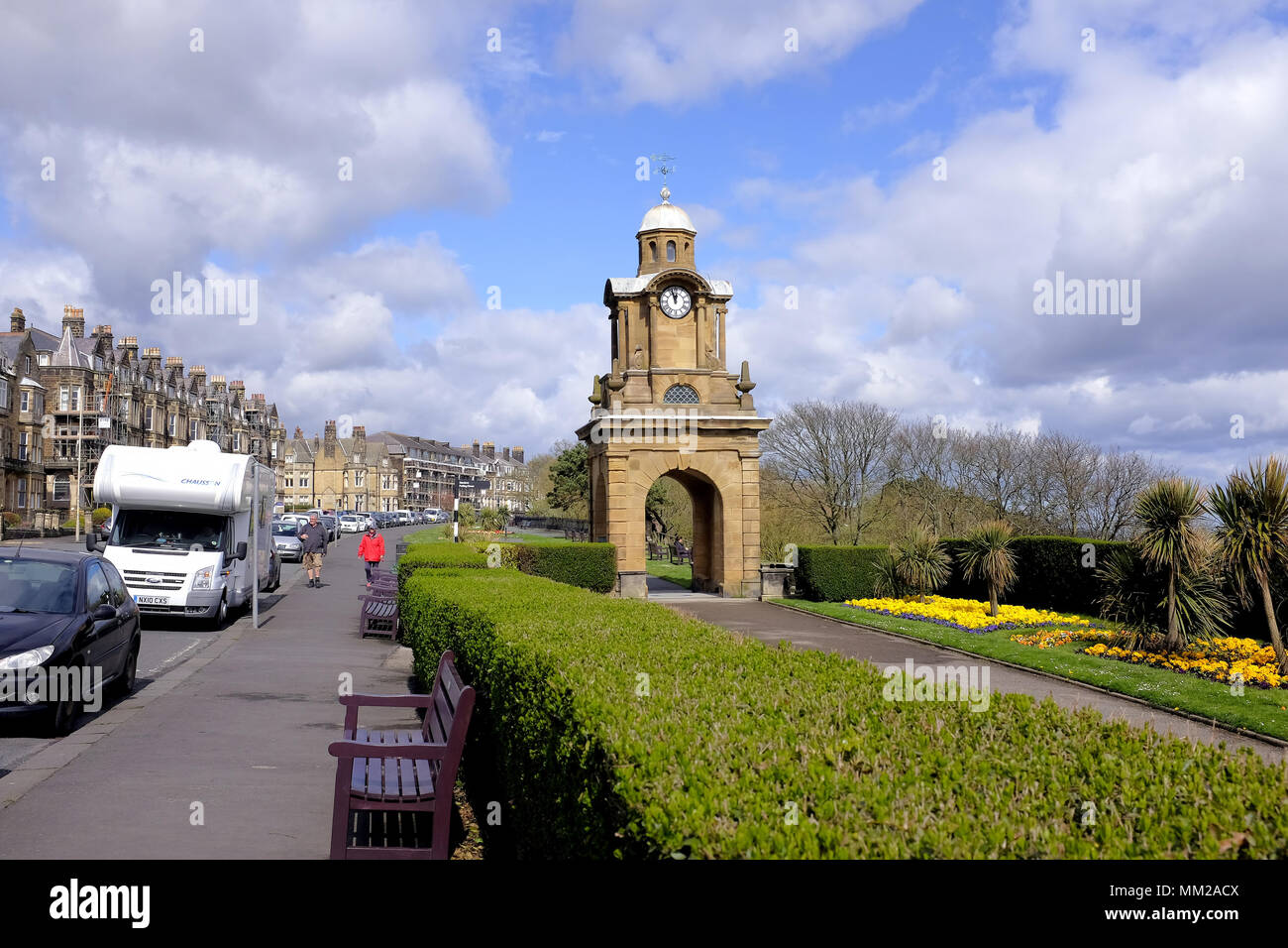 Scarborough, Yorkshire, UK. April  25, 2018.  Holidaymakers walking the Esplanade past the Holbeck clock tower and the South cliff gardens at Scarboro Stock Photo