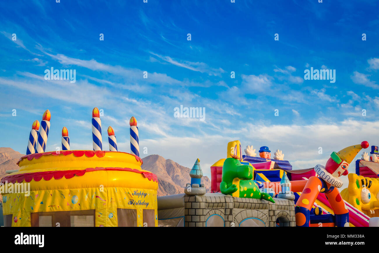 Colorful inflatable jumping castles for kids in the children's park under a blue sky. Stock Photo