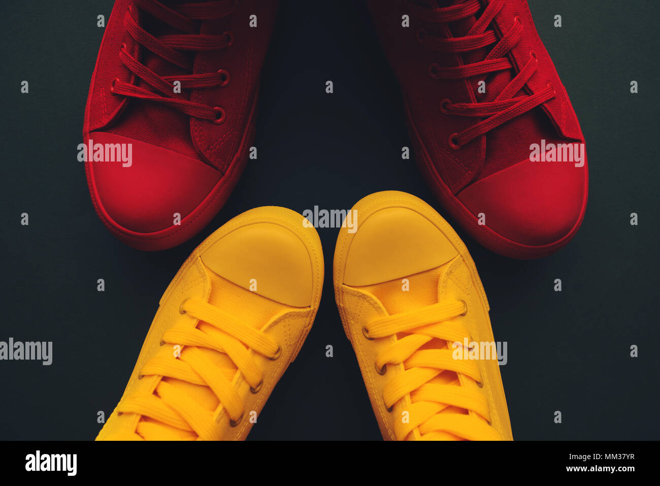 Young couple on a love date, conceptual image. Top view of two pair of casual sneakers, yellow and red, from above close to and facing each other like Stock Photo