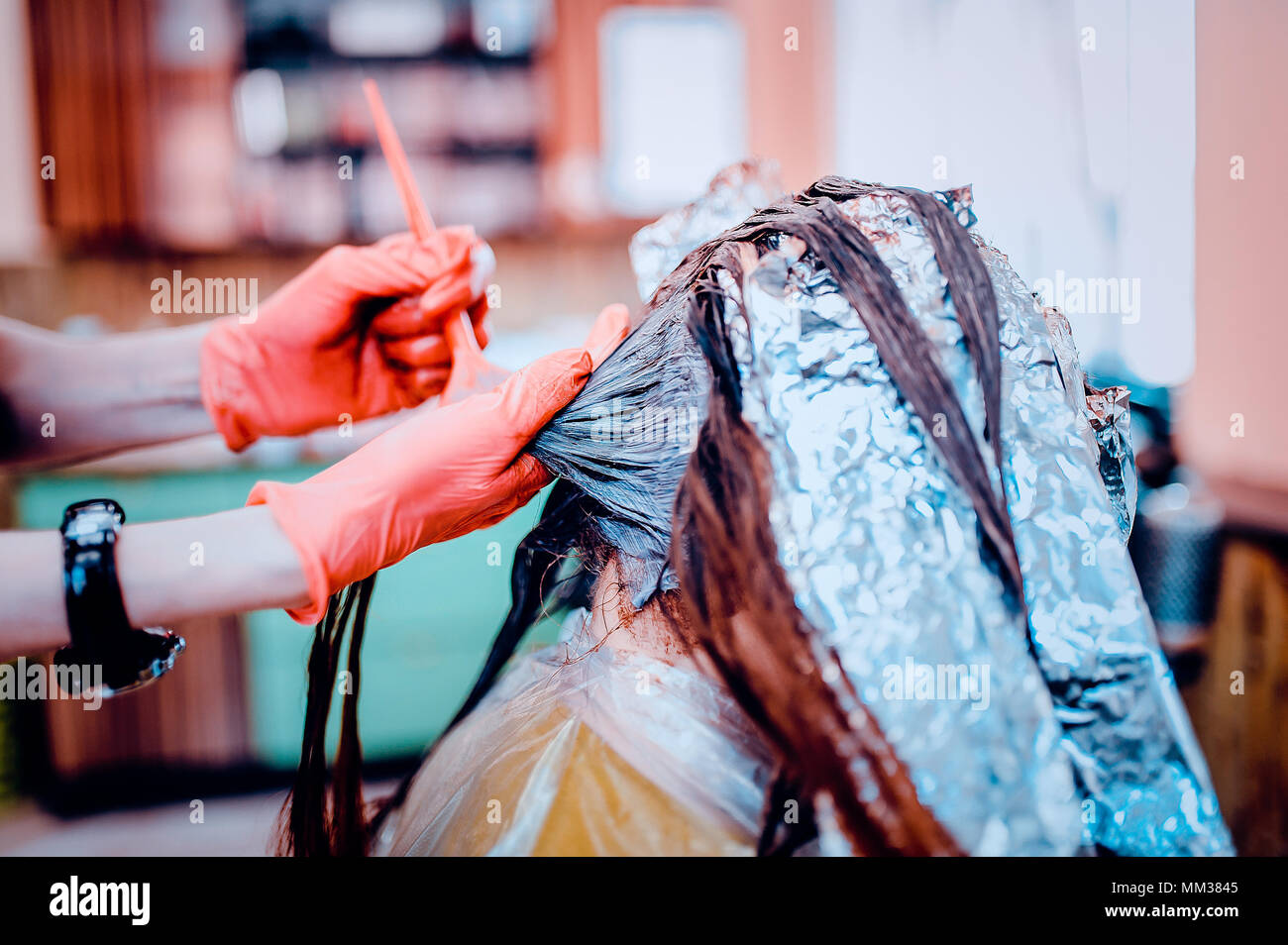 Woman in gloves is dying hair. hair dyeing. Toned image. Hair in foil