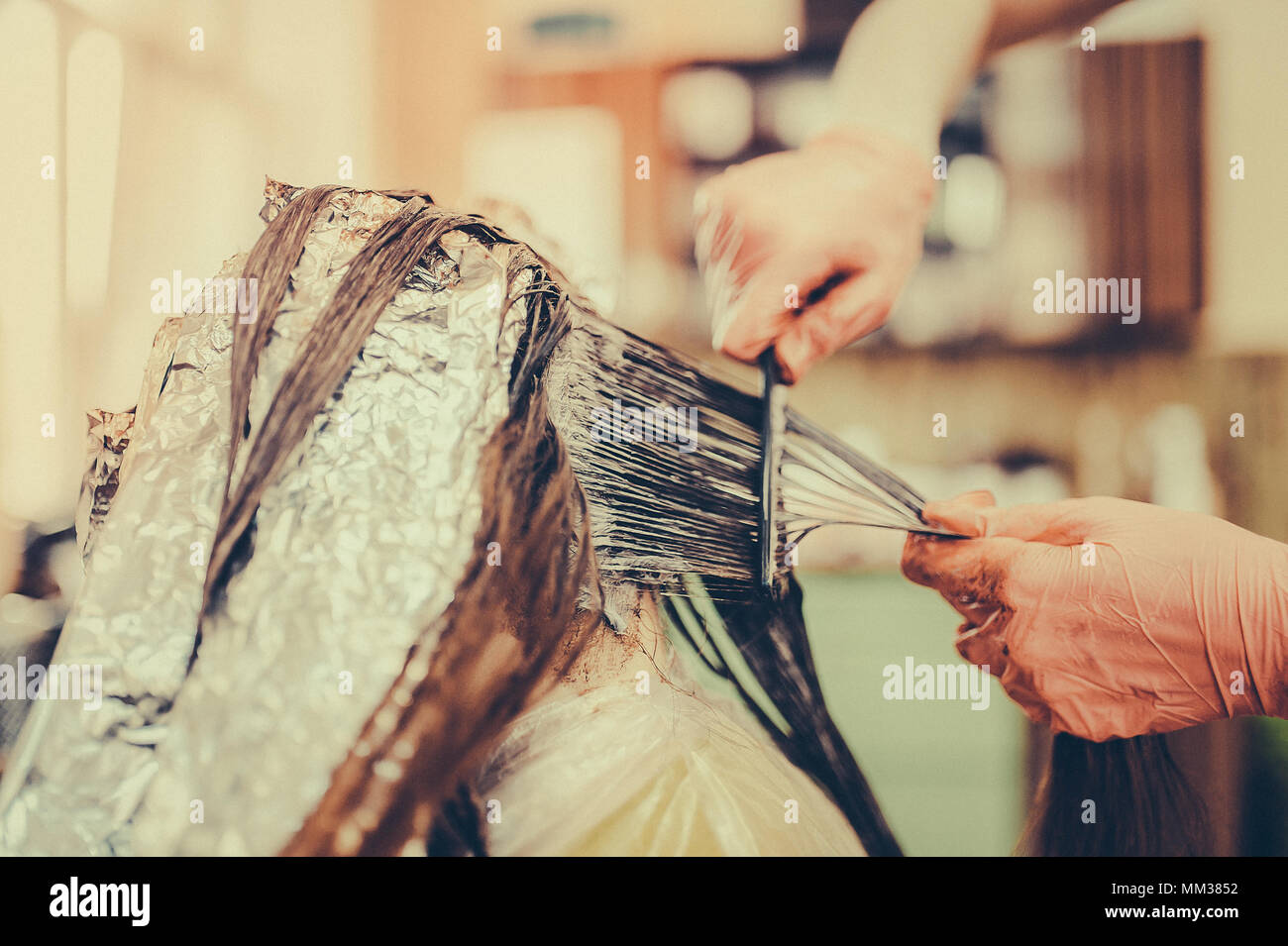 Woman in gloves is dying hair. hair dyeing. Toned image. Hair in foil