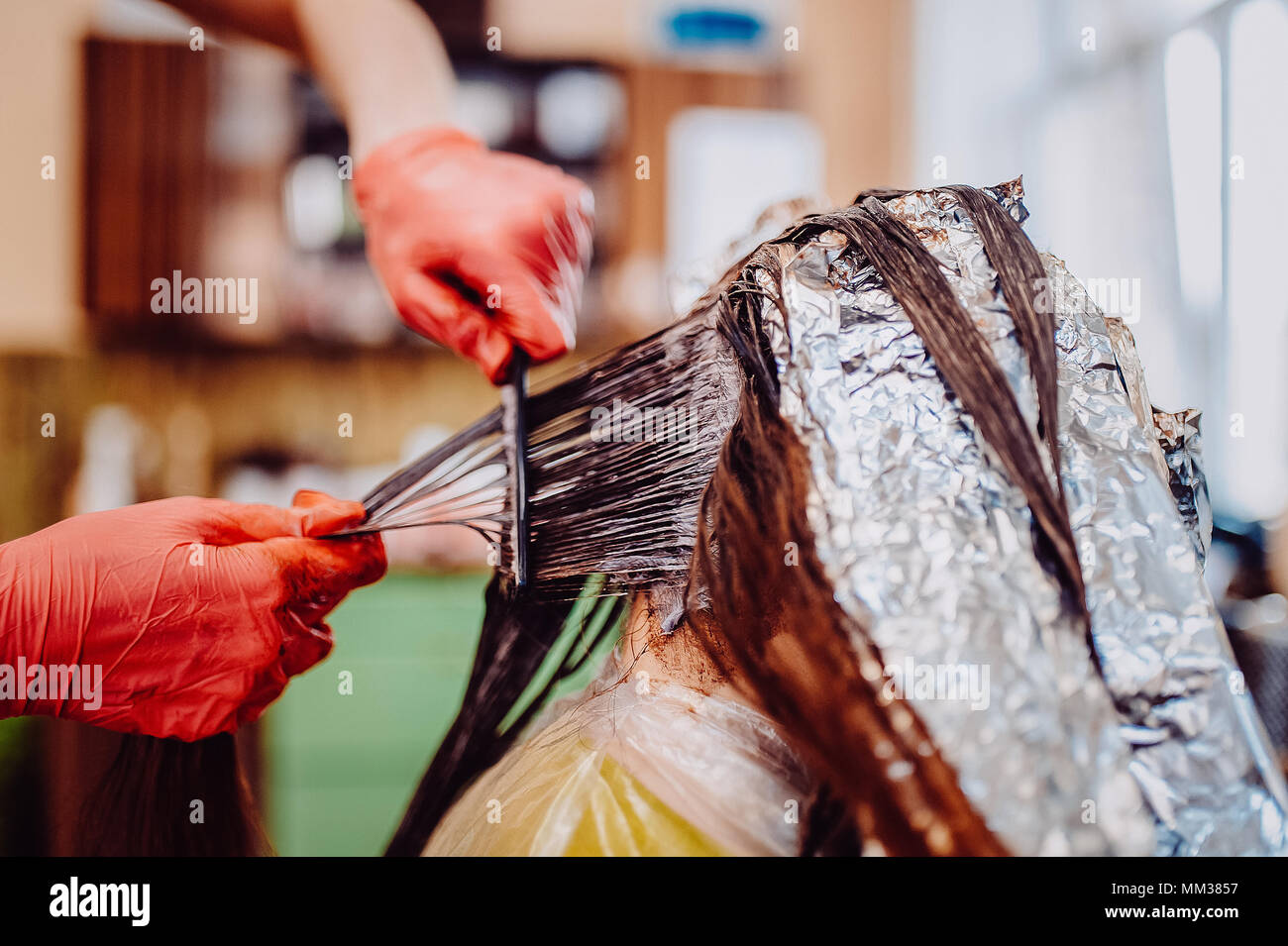 Woman in gloves is dying hair. hair dyeing. Toned image. Hair in foil