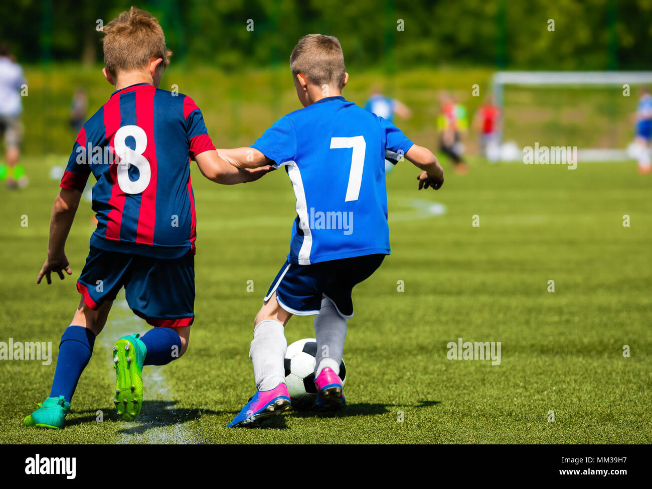 Two young soccer players kicking soccer ball on grass pitch. Youth sports competition between two school sports teams. Kids football tournament game. Stock Photo