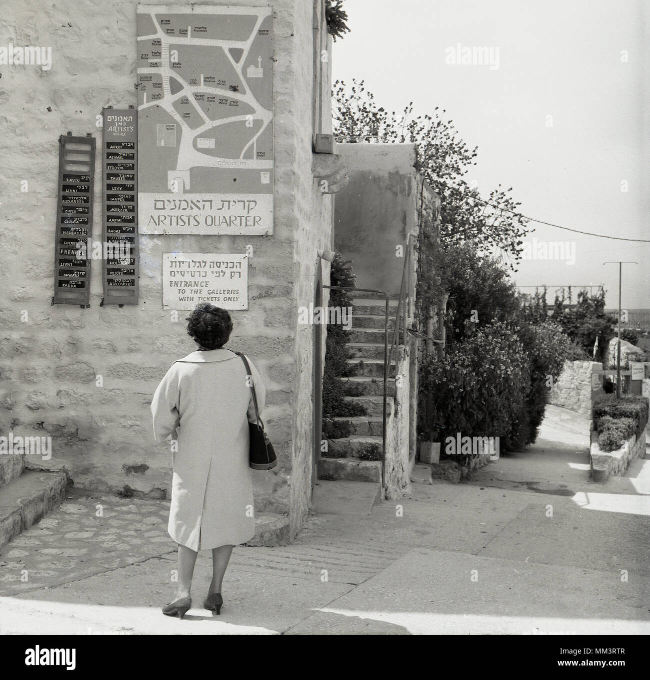 1950s, historical, western lady studies the sign and map on the side on a stone buidling for the Artists Quarter in the old city of Safed (Tzfat), Israel. In the 1950s and 1960s, Safed was known as israel's art capital and its reputation drew artists to the colony established in the Old City. Stock Photo
