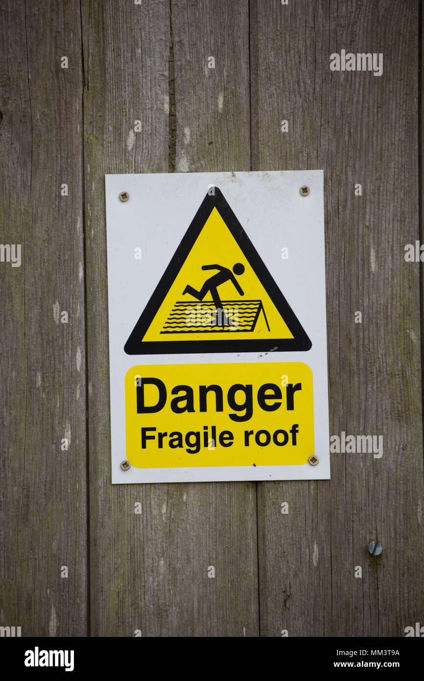 A sign warning of a fragile roof on a barn with a corrugated roof. Lancashire North West England UK Stock Photo
