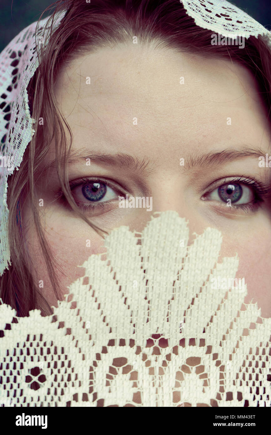 portrait of young woman with head covered by veil and lower face covered by decorative lace, violet eyes and tendrils of hair Stock Photo