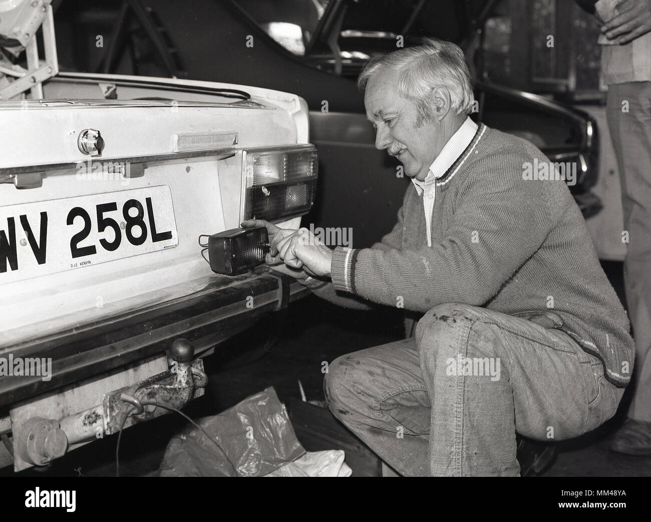 1970s, historical, a man attending an adult education class of car  maintenance or servicing, kneeling down while working on the back lights of a volvo motorcar, England, UK. Stock Photo