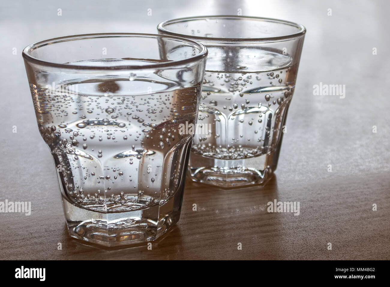 Two freshly poured glasses of sparkling water isolated on wood. Stock Photo