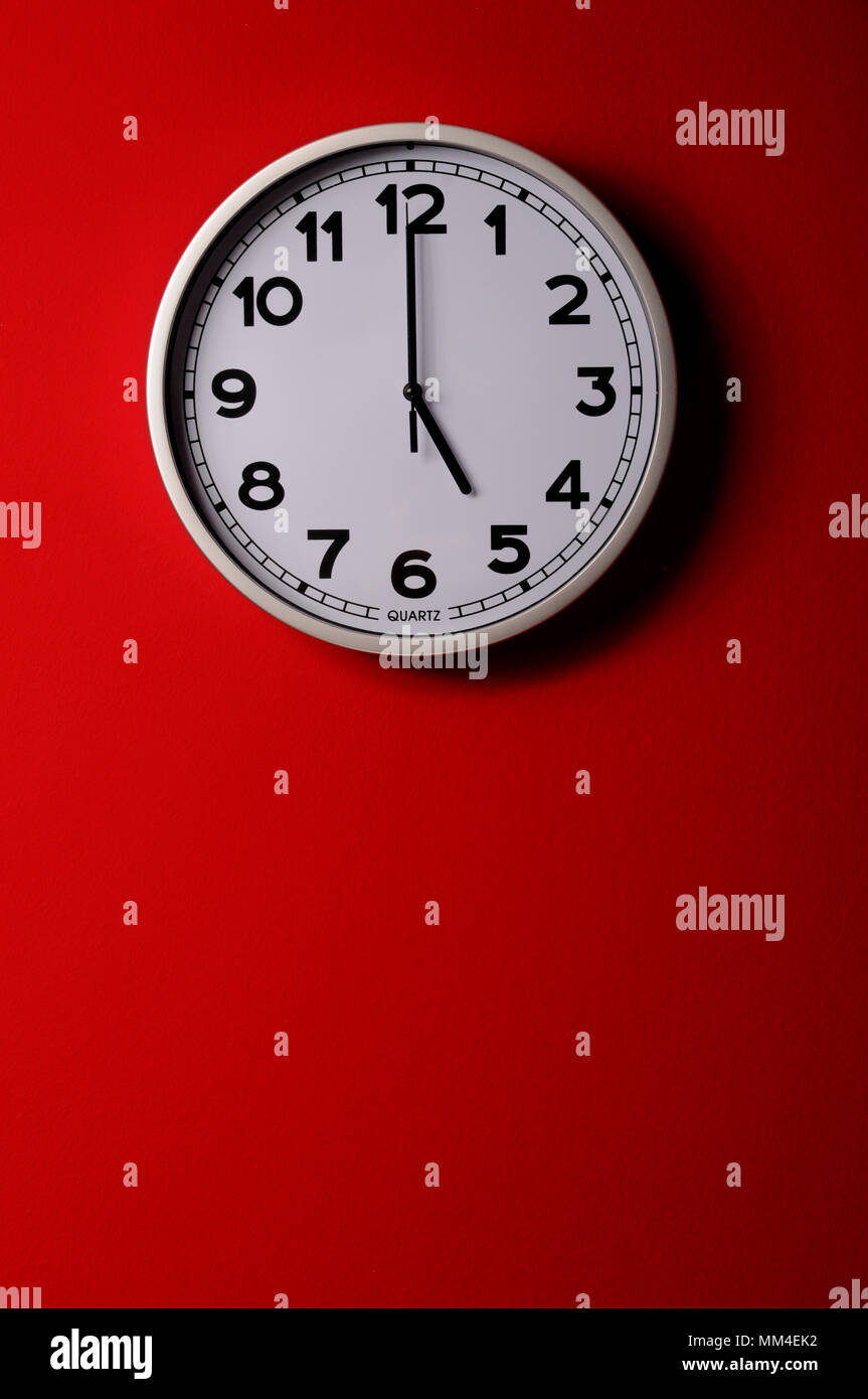 Five o clock. Clock hanging on the red wall. Stock Photo