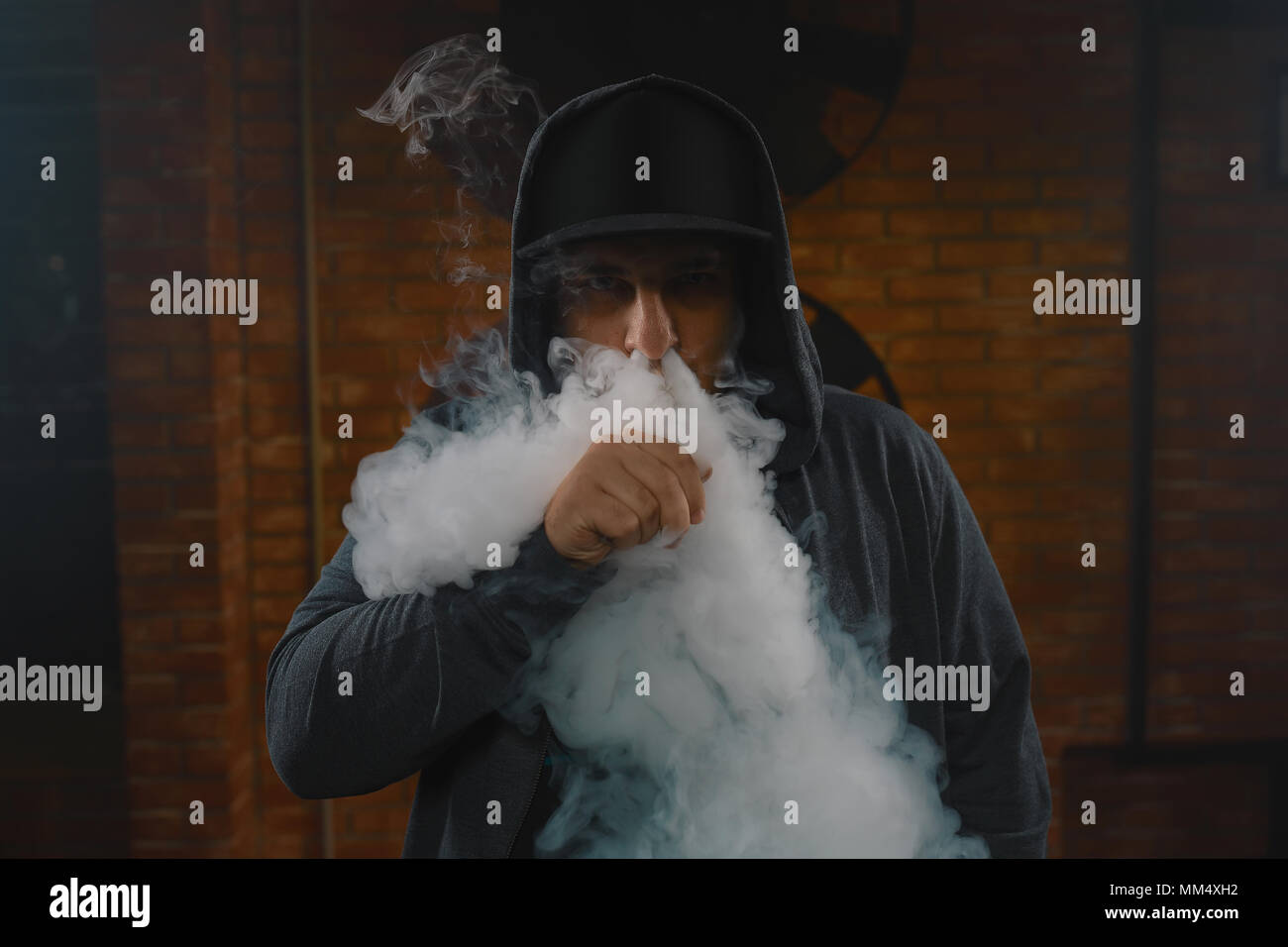 A cloud of vapor. Vaping man holding a mod. Brick background. Vape concept.  Young man with beard vaping an electronic cigarette. Vaper hipster smoke v  Stock Photo - Alamy