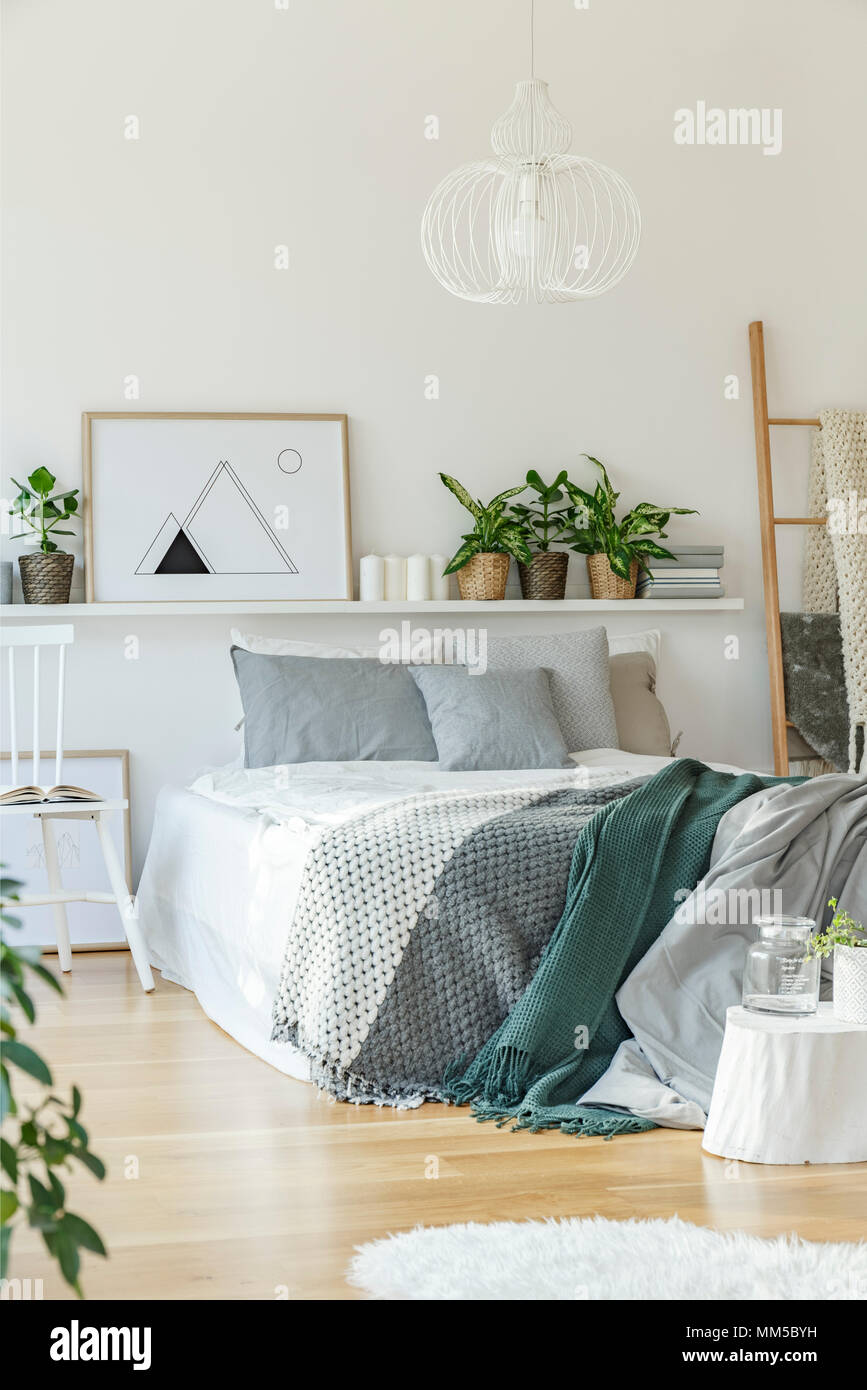 Bed, rug, shelf, chair and ornaments in bright bedroom interior Stock