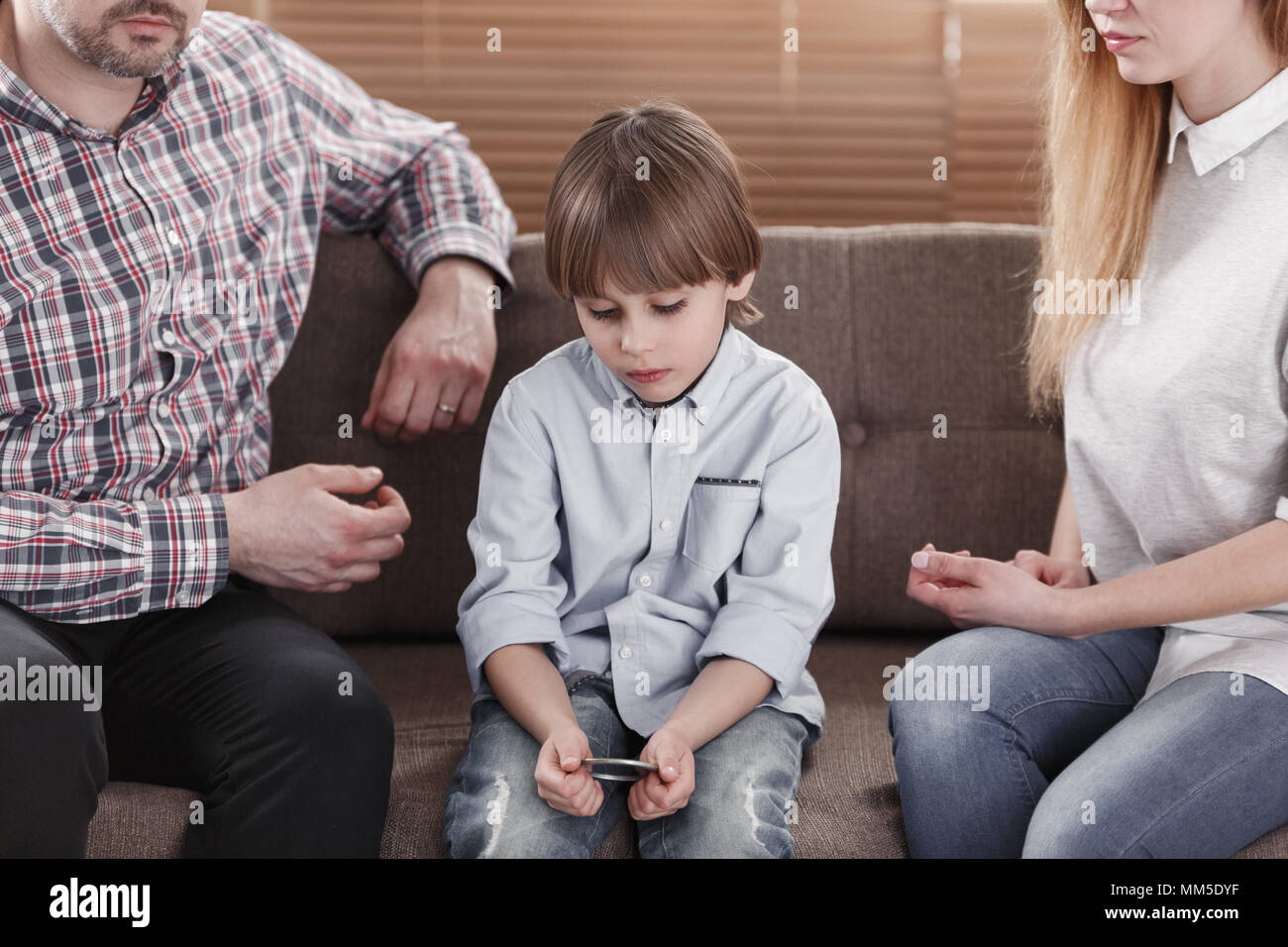 Close-up of sad boy with autism sitting between worried mother and father Stock Photo