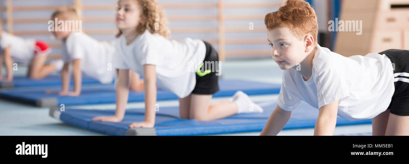 Young boy exercising on a blue mat during corrective gymnastics classes at school Stock Photo