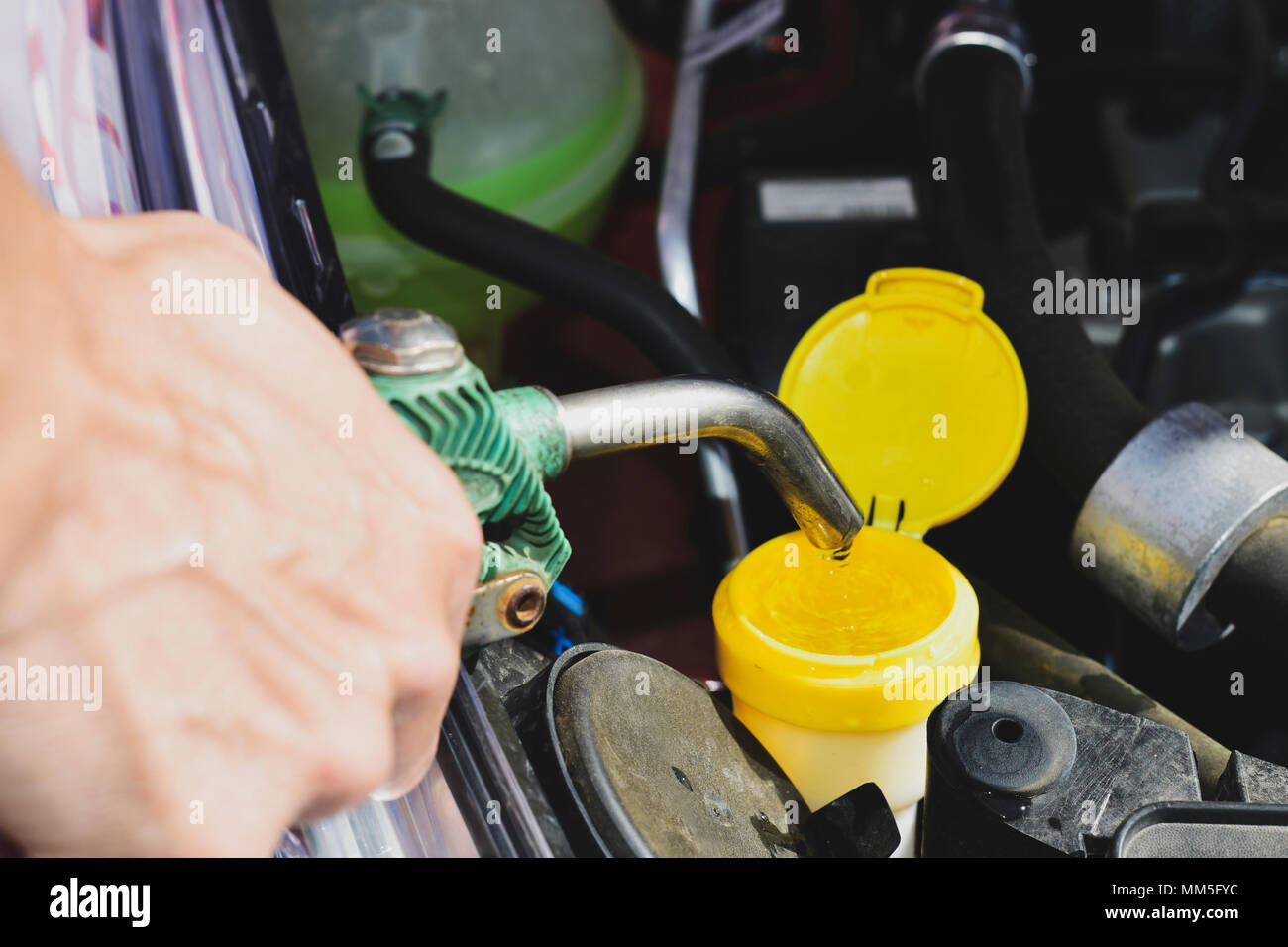 closeup of a young caucasian man filling the tank of windshield washer fluid of a car with water from a hosepipe Stock Photo