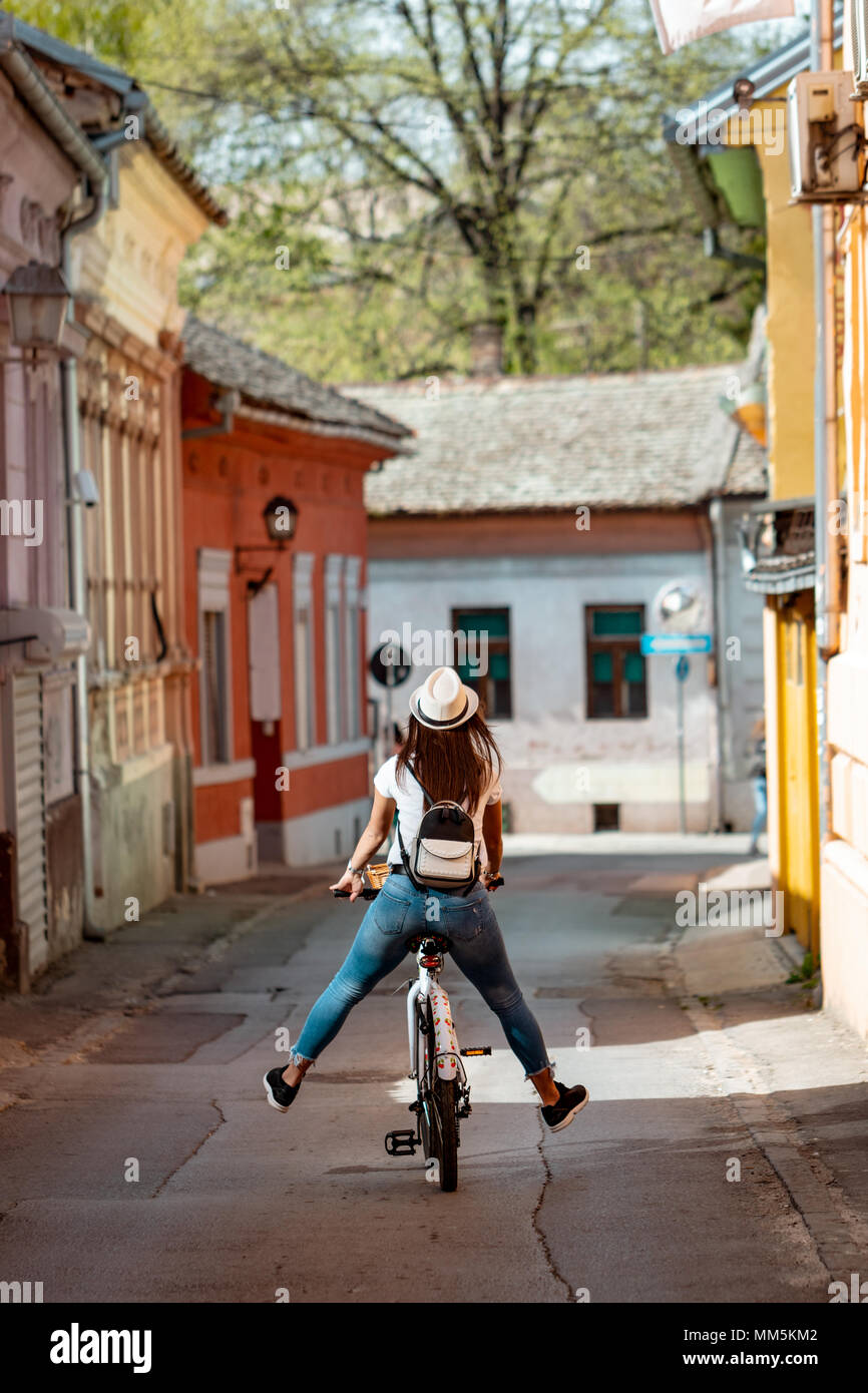 Rear view of a happy woman on bike cycling in summer sunny day, having fun of joy during outdoor activity. Stock Photo