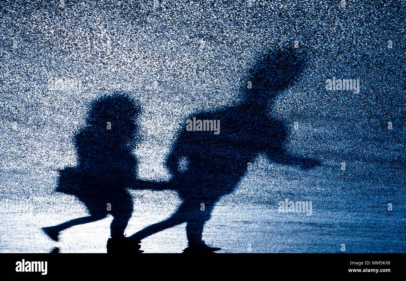 Defocused blurry shadow silhouette of young couple holding hands while walking on asphalt road in the night Stock Photo