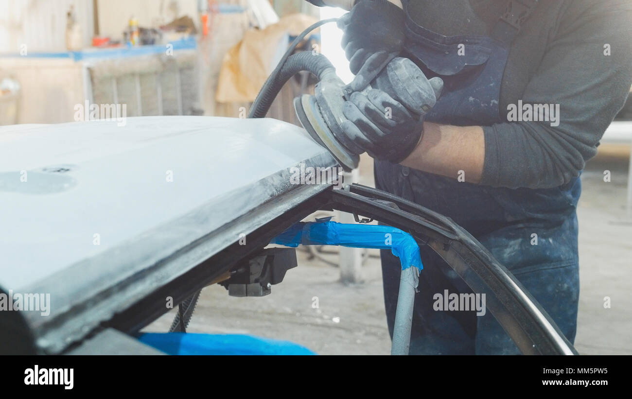 Man worker in car workshop polishing the car - preparing for painting Stock Photo