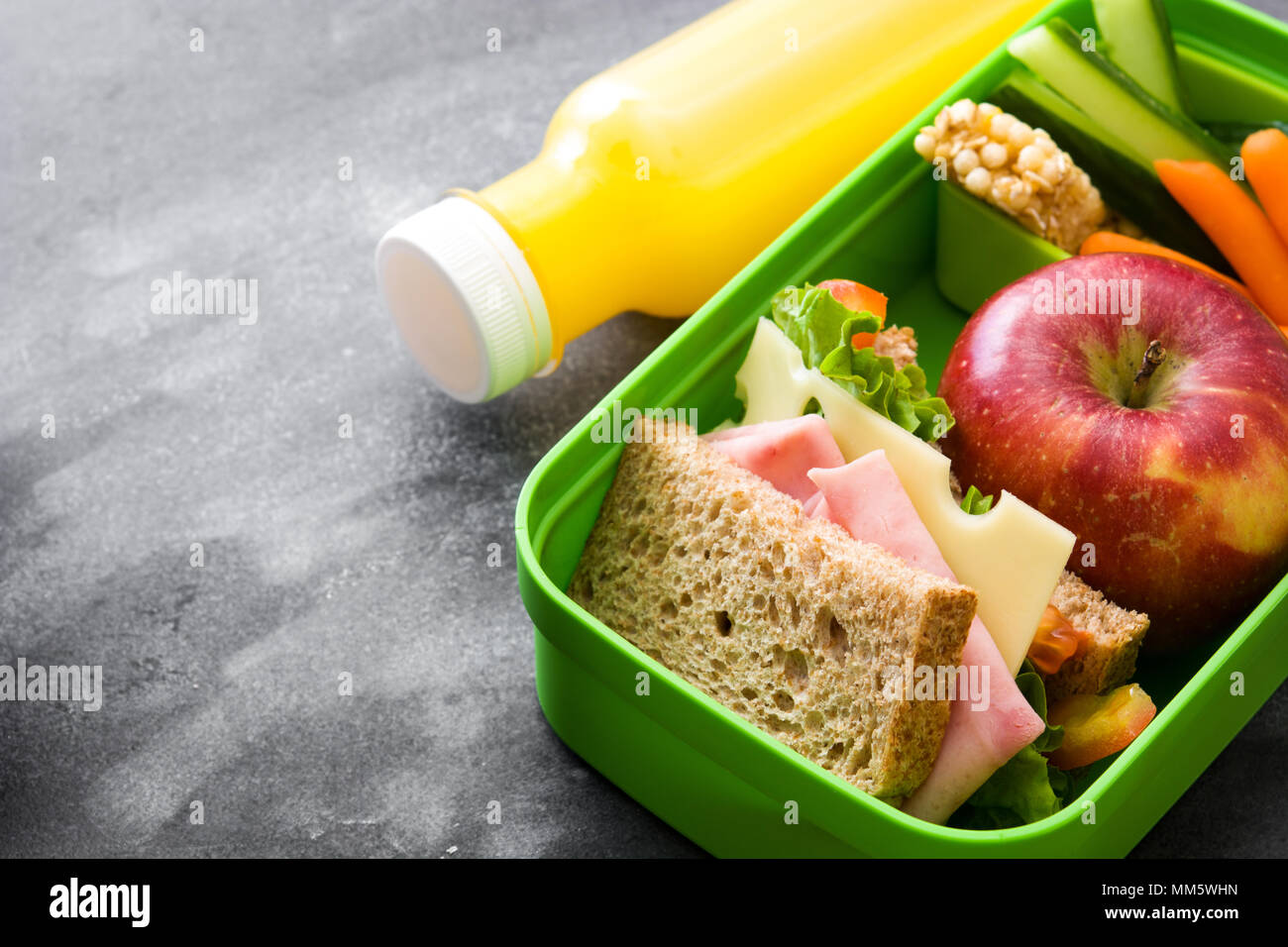 Healthy school lunch box: Sandwich, vegetables ,fruit and juice on black stone Stock Photo