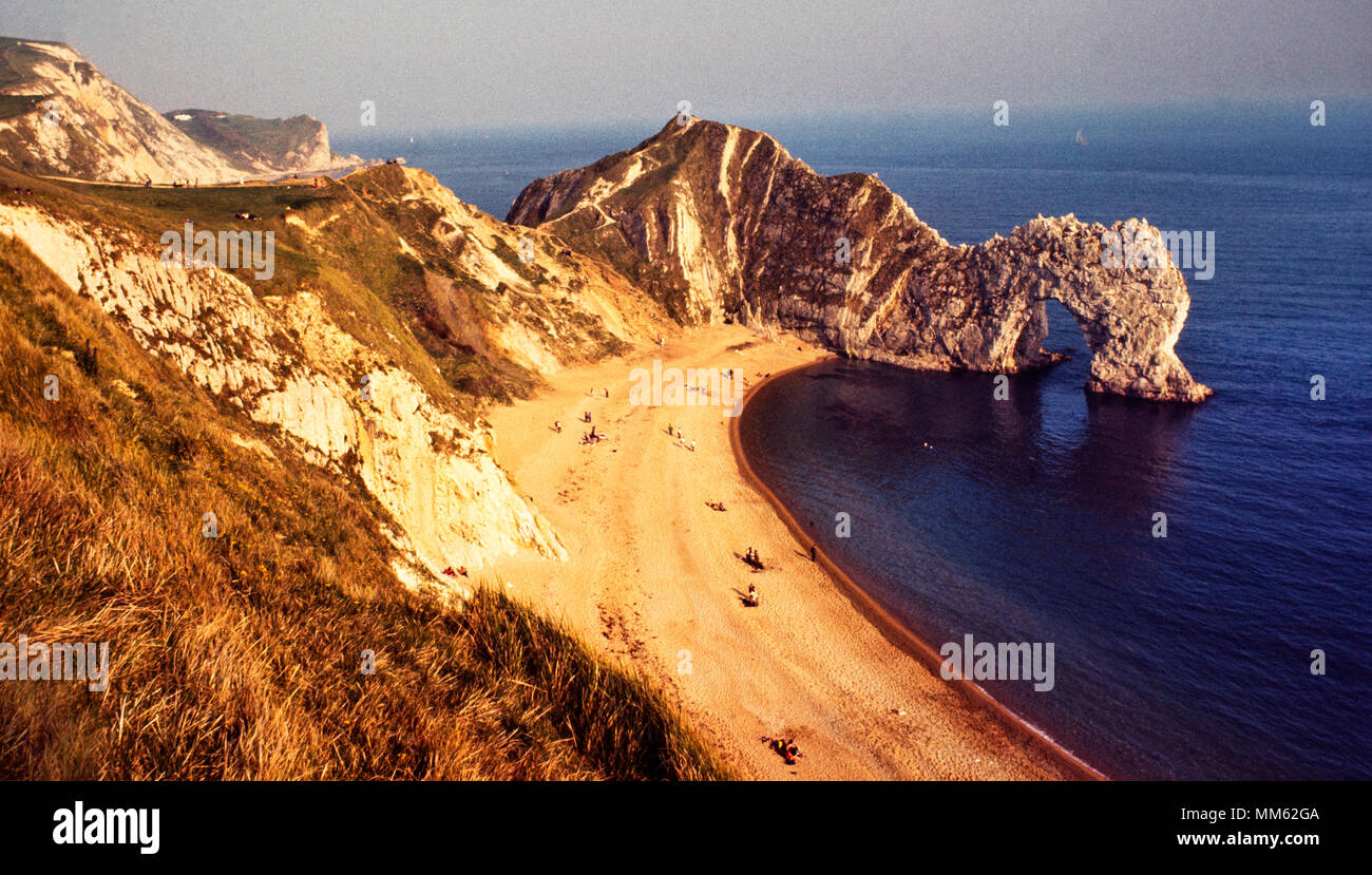Lulwoth Cove showing Durdle Door photographed in 1973 Scan made in 2018 Lulworth Cove is a cove near the village of West Lulworth, on the Jurassic Coast World Heritage Site in Dorset, southern England. The cove is one of the world's finest examples of such a landform, and is a tourist location with approximately 500,000 visitors a year, of whom about 30% visit in July and August.It is close to the rock arch of Durdle Door and other Jurassic Coast sites. Stock Photo
