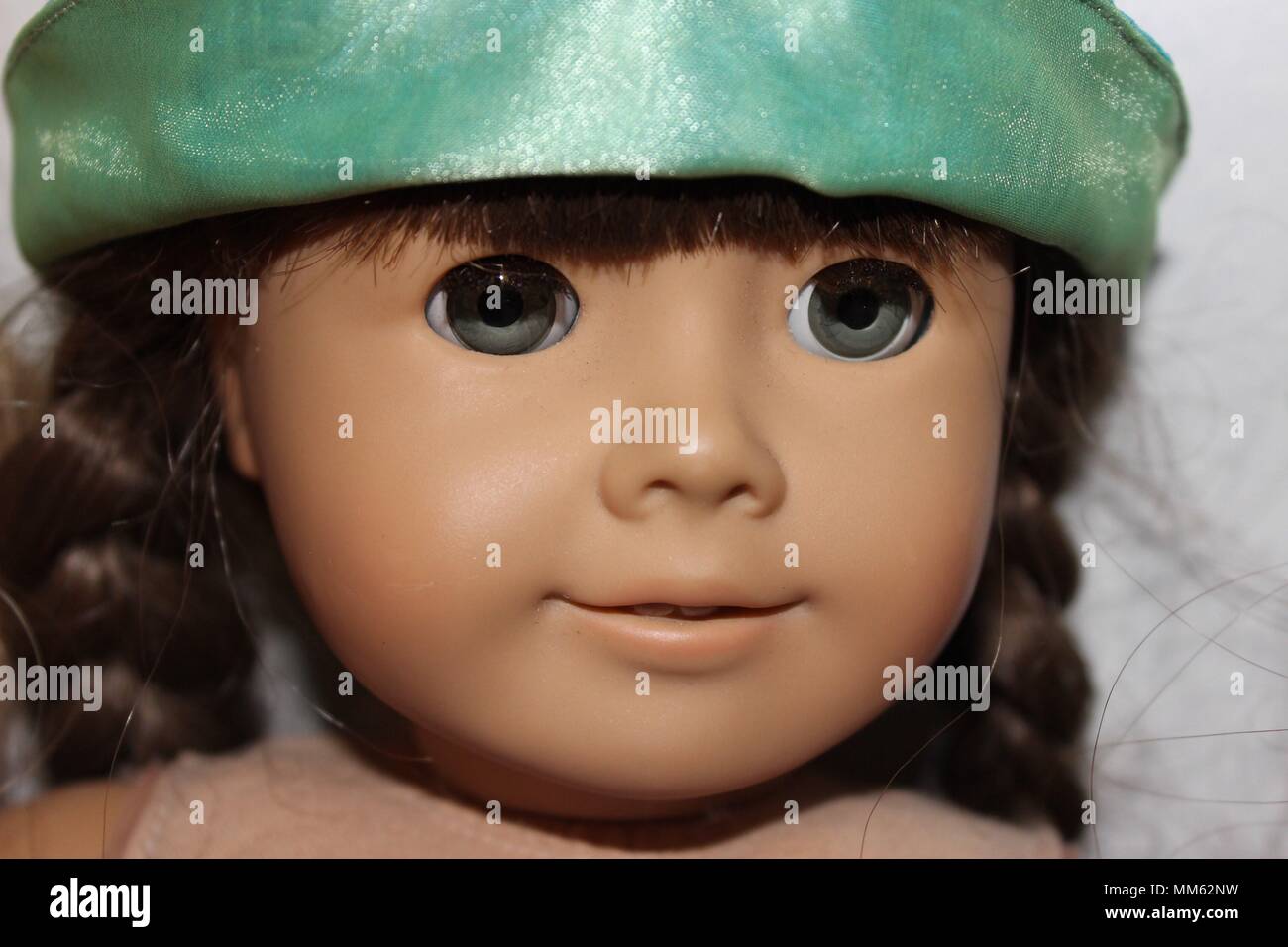 American Girl Doll (no brand shown) with a partially pictured green hat against a white background. Stock Photo