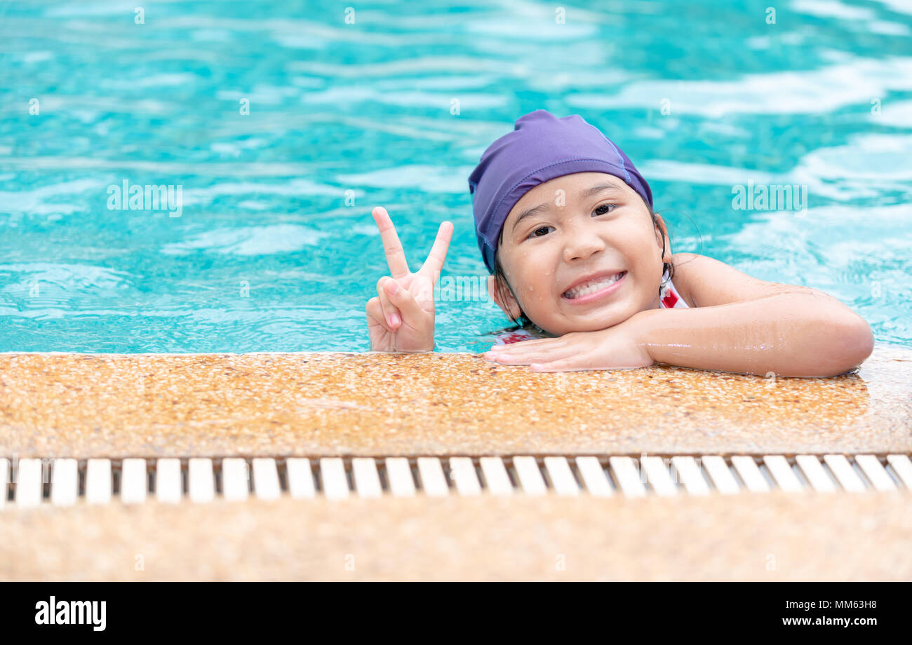 Happy little girl smile and wear swimming cap in outdoor swimming pool on summer. Kids learn to