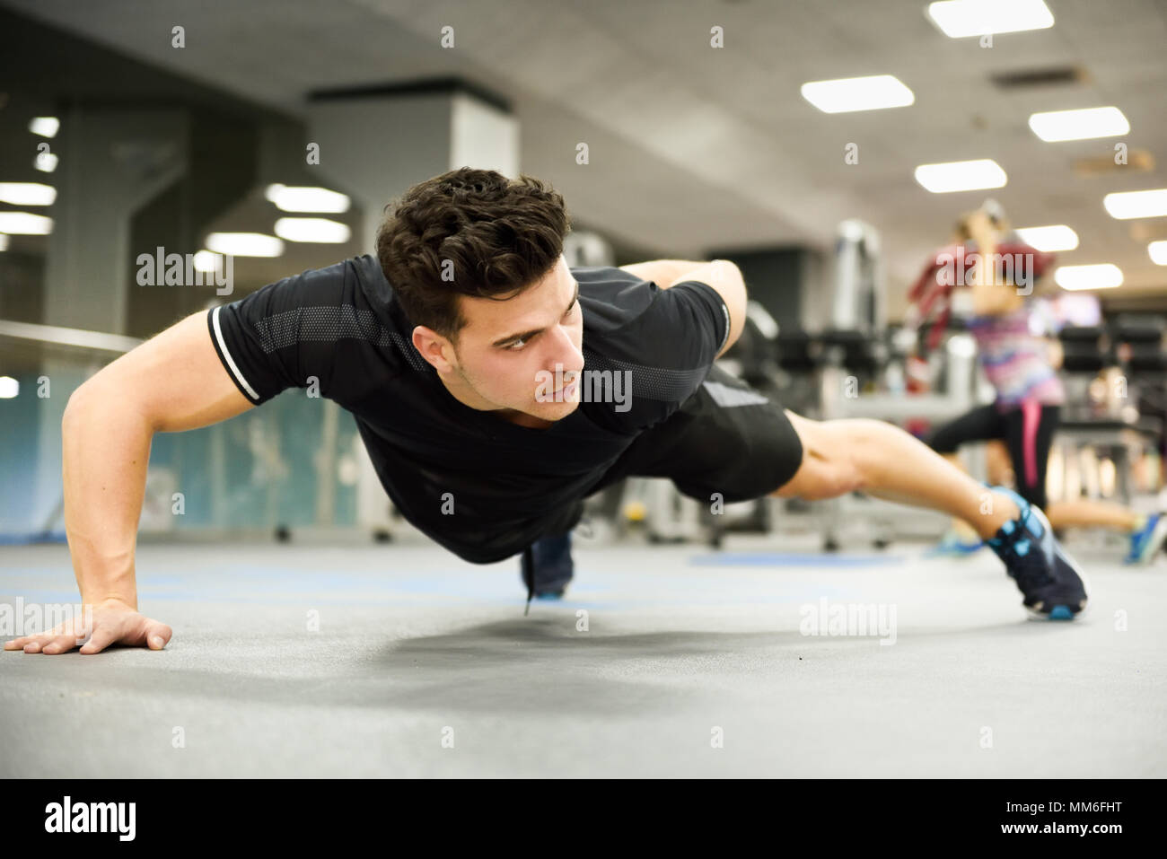Attractive man doing pushups in the gym. Guy wearing sportwears clothes. Stock Photo