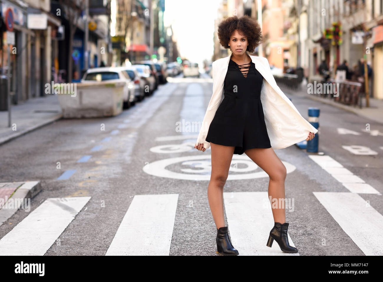 Young black woman with afro hairstyle walking on a crosswalk in an ...