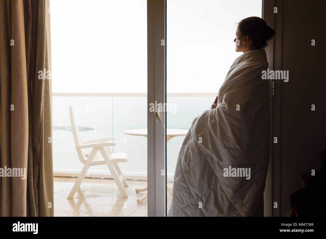 Silhouette of Womanin white blanket Looking out the Window at Home Stock Photo