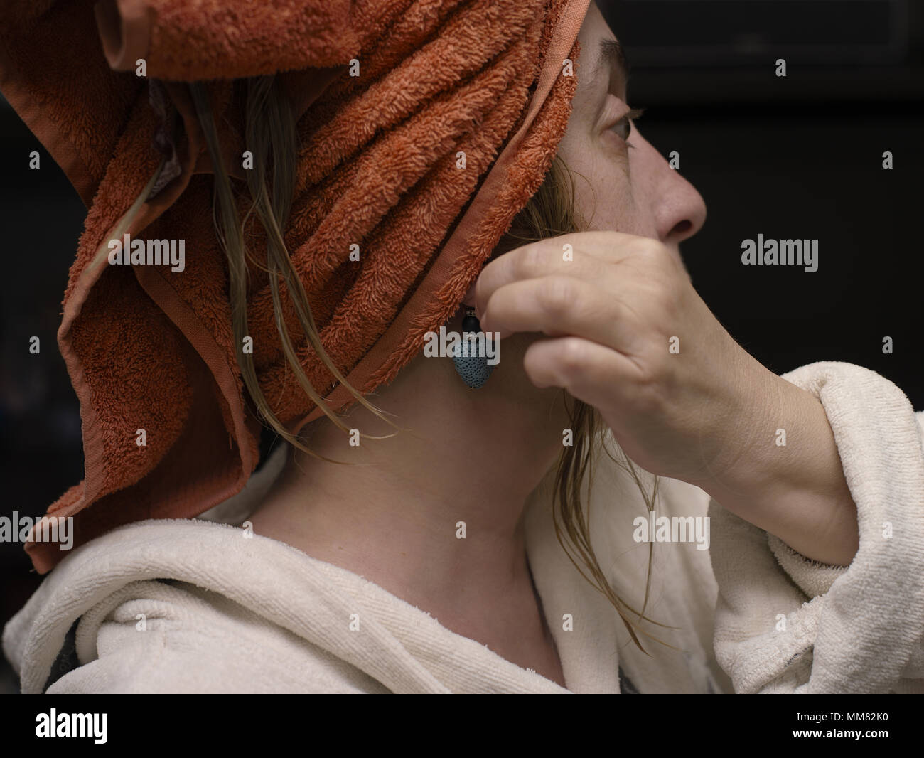 A woman with a bath towel on a hand putting earrings, indoor closeup