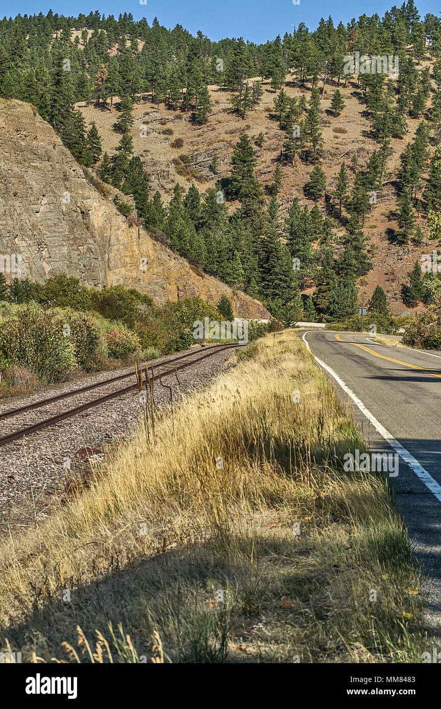 From left to right is a concrete barrier for the interstate, railroad tracks, and a two-lane road.  All of them curve with a great view of the mountai Stock Photo