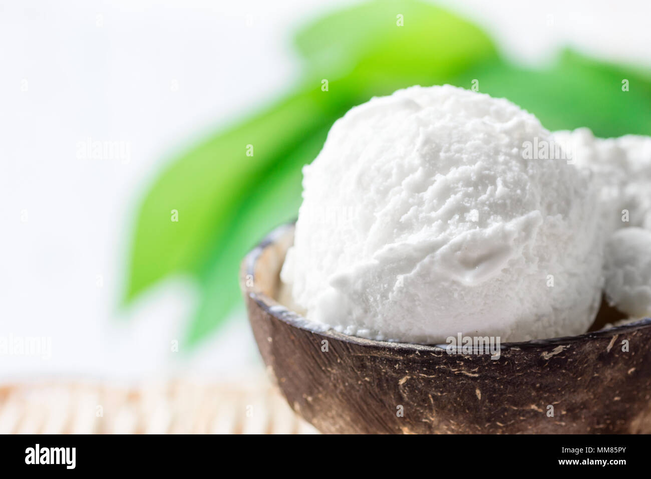 Delicious Vegan Coconut Ice Cream in Bowl on Wicker Table. Green Palm Leaves Tropical Plants Background. Plant Based Diet Healthy Dessert Superfoods.  Stock Photo