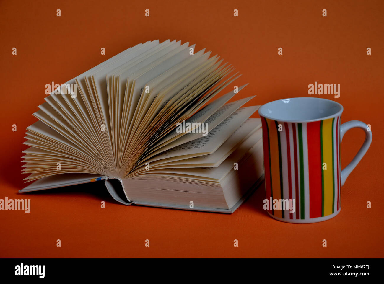 Coffee cup and open book forming a fan on orange background Stock Photo