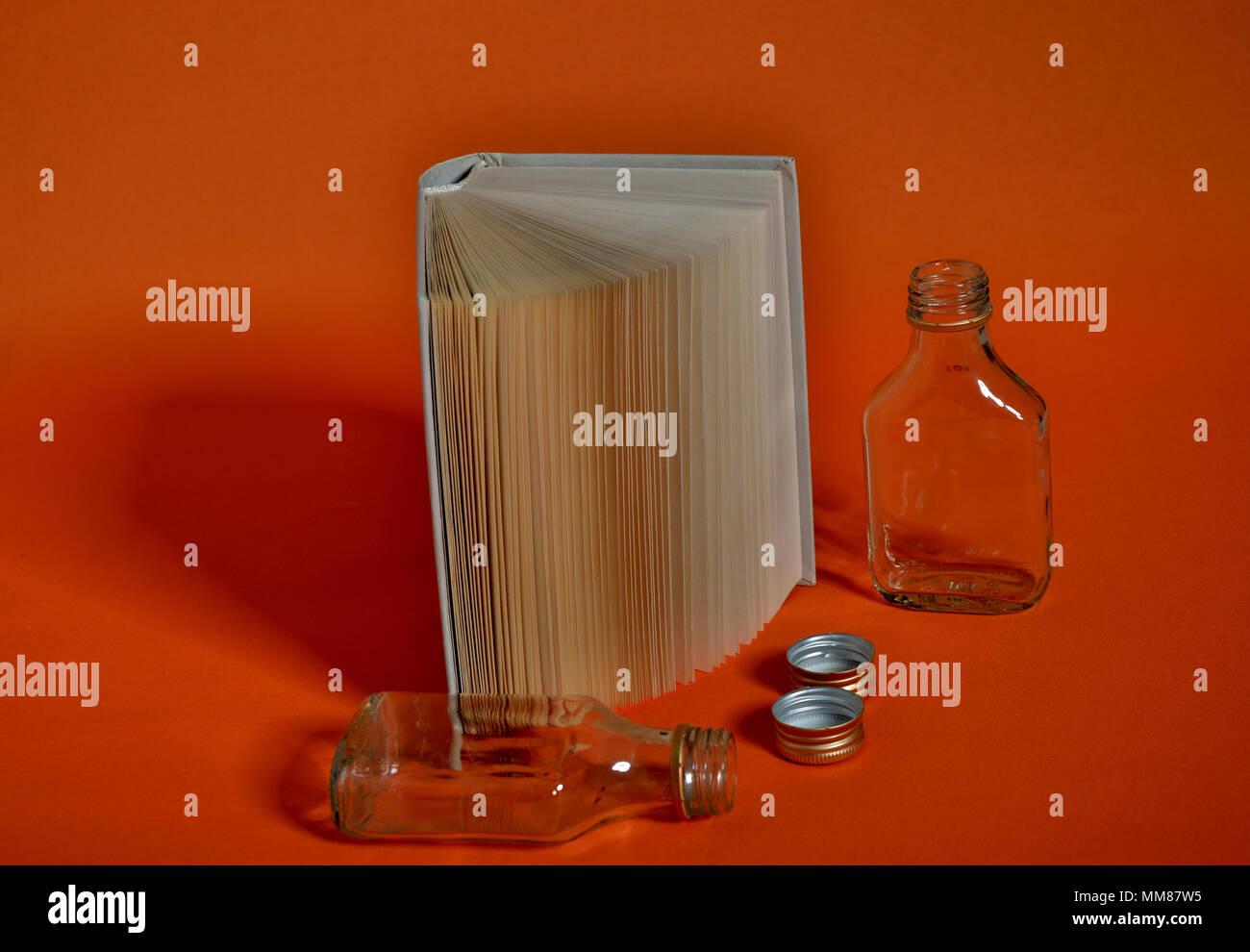 Open standing book and liquor bottles on orange background Stock Photo