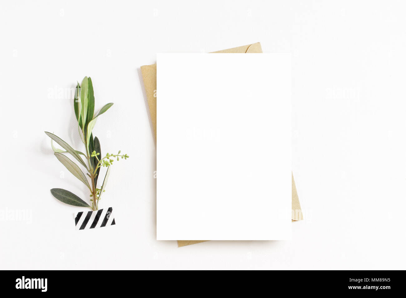 Feminine stationery, desktop mock-up scene. Blank greeting card, craft envelope, washi tape and with olive branch.White table background. Flat lay, top view. Stock Photo