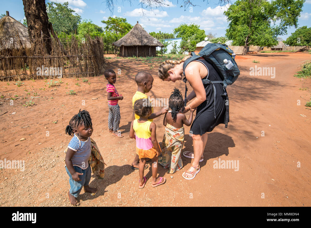 Group of young Zambian children gather around young Caucasian woman to look at camera, Mukuni Village, Zambia Stock Photo