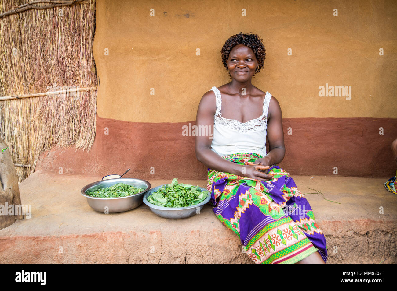 Zambian woman sits next to two bowls of fresh greens that she just prepared, Mukuni Village, Zambia Stock Photo