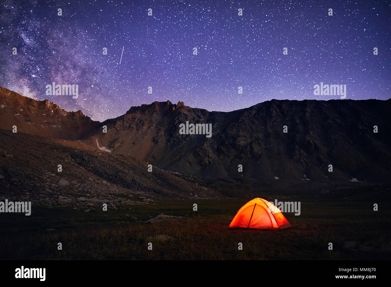Orange tent glows under night sky full of stars and Milky way in the mountains in Kazakhstan Stock Photo