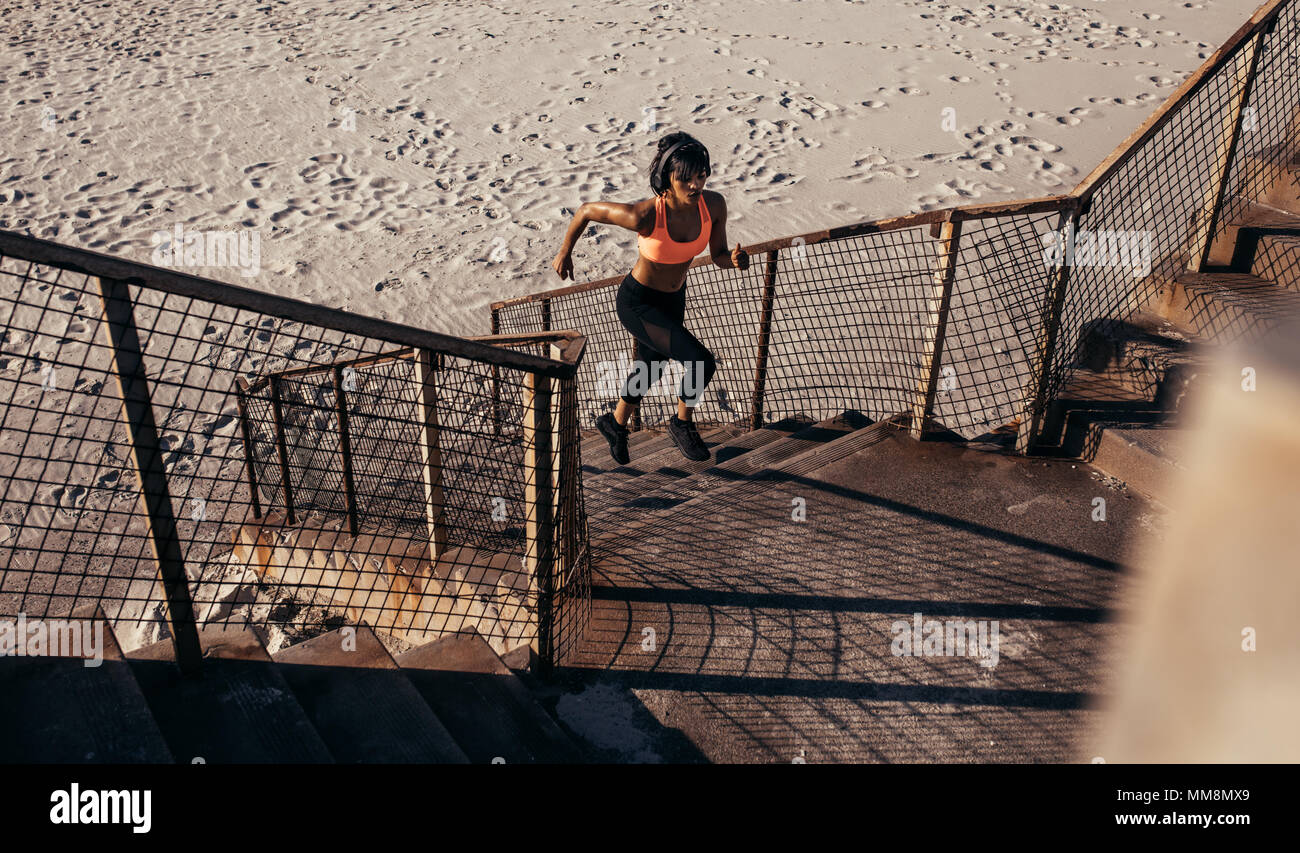Athletic woman runs up the steps on the beach. Athlete in sportswear training on concrete steps. Stock Photo