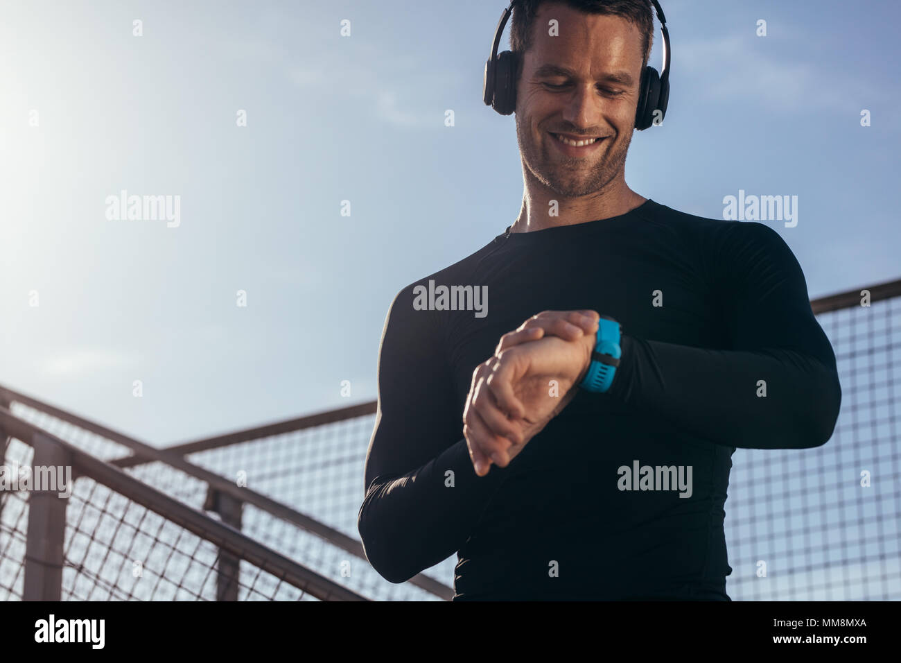 Man standing outdoors with headphones using a smartwatch to monitor his progress. Male athlete