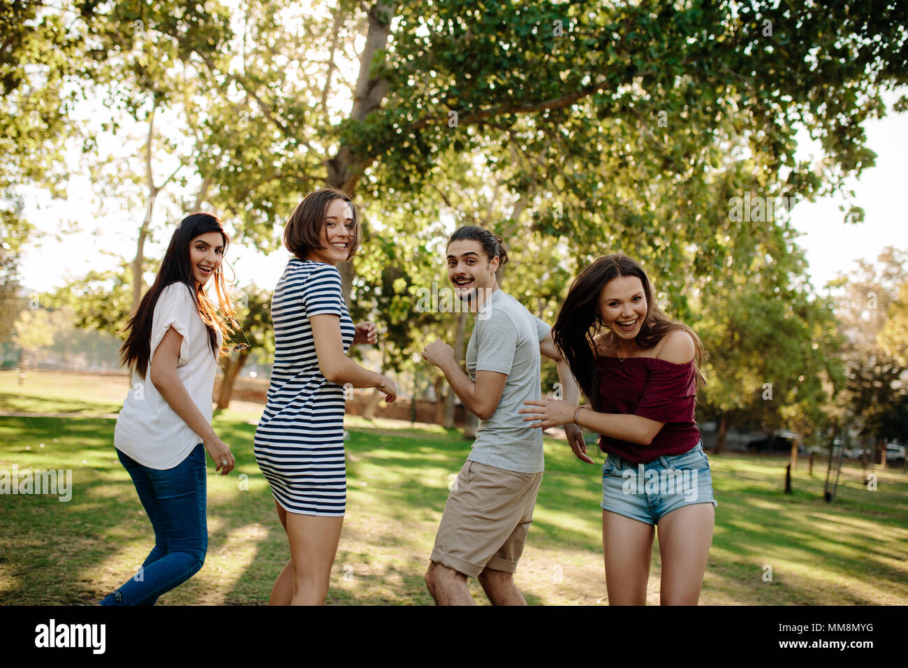 Group of four young friends looking back and laughing while walking in the park. Young man and woman enjoying a summer day at park. Stock Photo